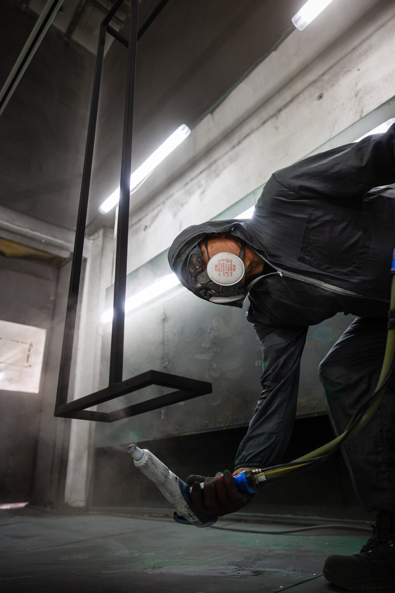 Pracownik maluje proszkowo metalowy element w ochronnym kombinezonie